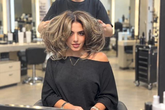Ash-toned layered hair being styled in front of a mirror