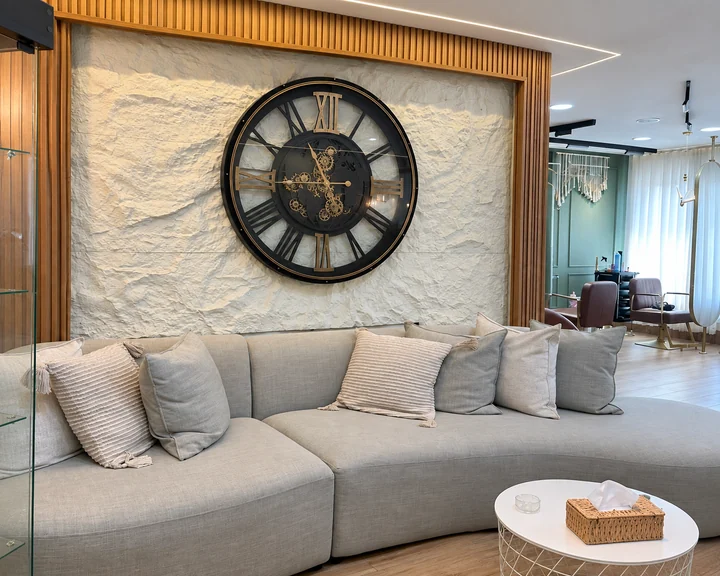 The salon lounge with a pale sofa, stone wall and oversized clock